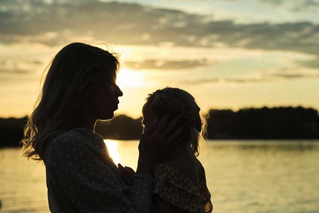 silhouettes of a mother and child embracing at a lake during sunset evoke a sense of peace
