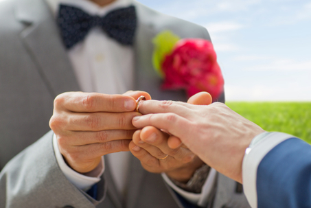 Close-up of man putting a ring on husband's finger.