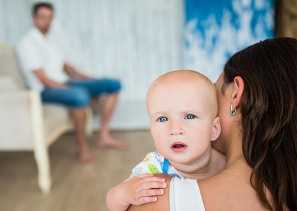 A woman holding a baby with a man in the background