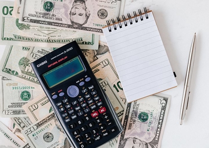 A calculator, dollar bills, a booklet, and a pen