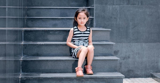 A young girl is sitting on gray stone steps.