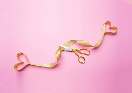 Gold ribbon, scissors, and two heart shapes on a pink surface.