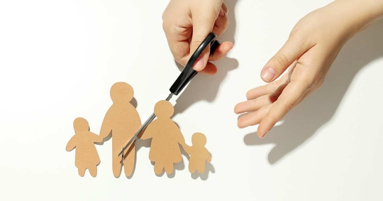 Scissors are cutting out paper figures of a family.