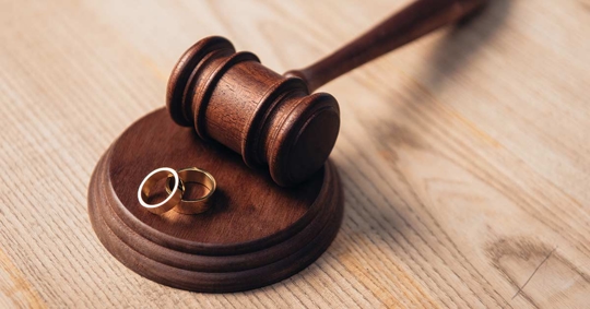 A wooden judge's gavel rests on a stand, with two wedding rings on top