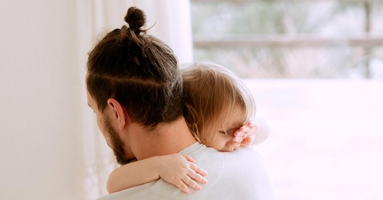 A man is holding a young girl close, cradling her on his shoulder.