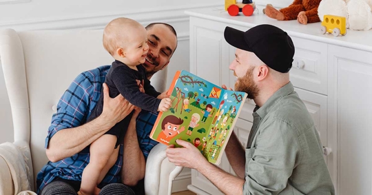 Two men are reading a book to a baby.