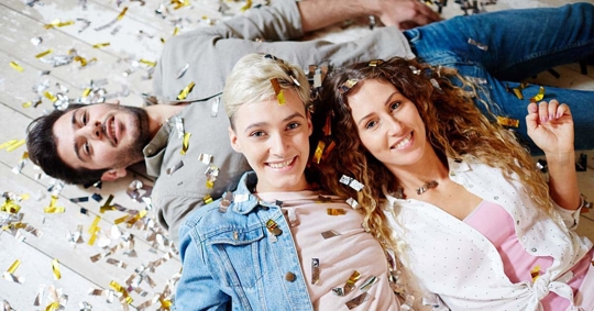 Three people are lying on a floor covered in gold and silver confetti.