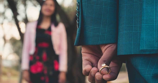 A teal plaid suit jacket. A hand holding a diamond ring.