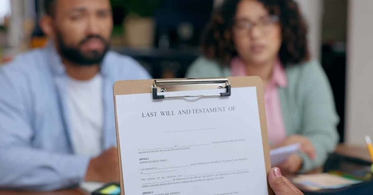 A clipboard with a legal document, likely a Last Will and Testament, being reviewed by a couple.