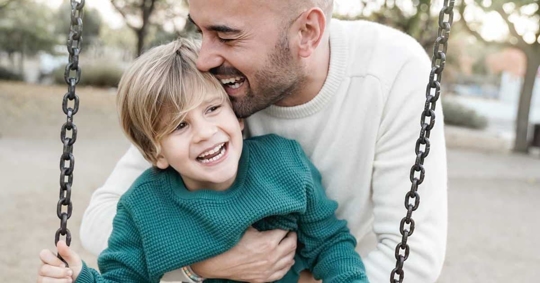 A happy father and young son are on a swing set.