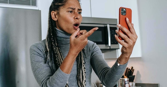 A person in a gray sweater is looking at a red phone.