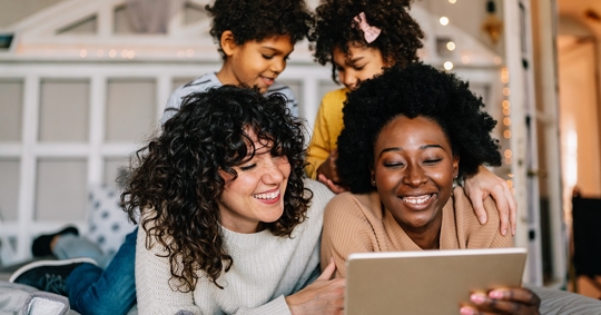 Three women and two children are gathered, looking at a tablet.